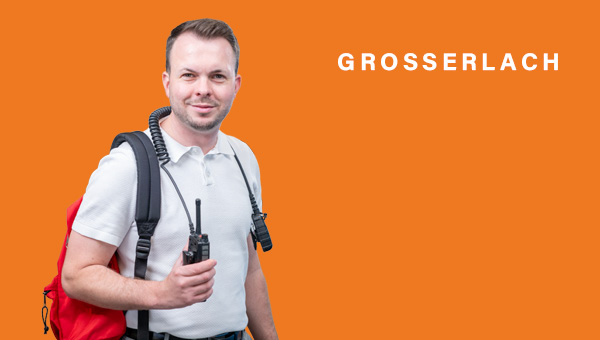 Kevin Dispan mit rotem Rucksack über der Schulter, um den Hals ein Funkgeräte